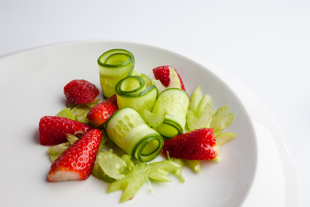 Cucumber strawberries and celery slices on white plateの写真素材