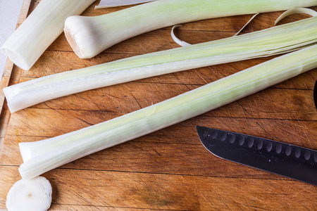 Cutting fresh leek on wooden cutting board with knifeの写真素材