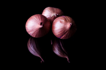 Three shallot onions with shell on black background with reflectionの写真素材