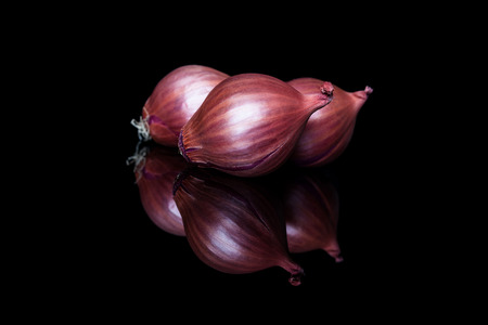 Three shallot onions with shell on black background with reflection from sideの写真素材