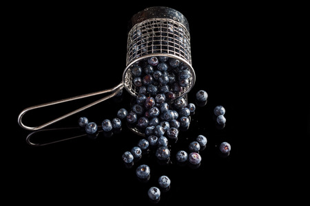Blueberries spilled from steel cup strainer on black background from side high angleの写真素材