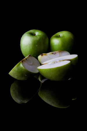 Two whole green apples and one sliced on black background directly from side with reflection verticalの写真素材