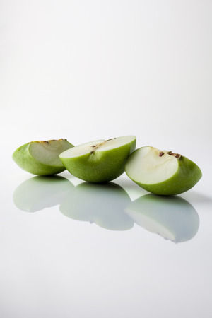 Sliced green apple half and two quarters on white background from side with reflection verticalの写真素材