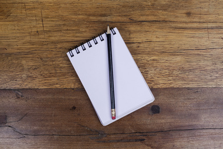 White sheets notebook with spiral in the center of the wooden dark brown table with black pencil on...