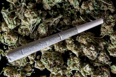 Medical cannabis rolled joint on dried marijuana buds on black background from above
