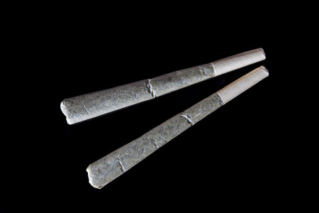 Two medical cannabis rolled joints on black background directly from above