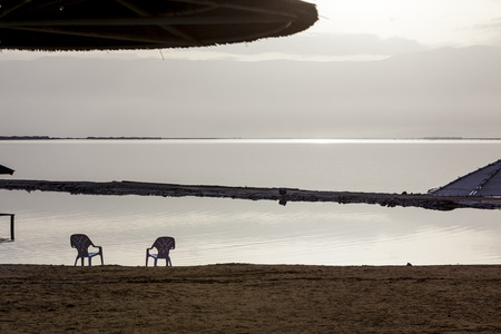 Two white plastic chairs and sunshades at lonely beach in the early morningの写真素材