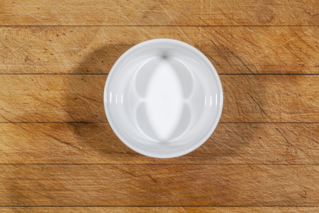 Small white deep bowl on wooden cutting board from above