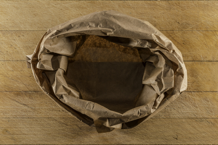 Brown paper empty sack on used wooden cutting board directly from above closeupの写真素材