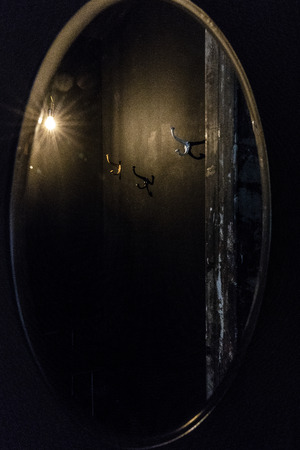 Black dressing room reflection in the oval mirror with gold frame with silver and gold pegs on the wall peeling door cant light bulbの写真素材