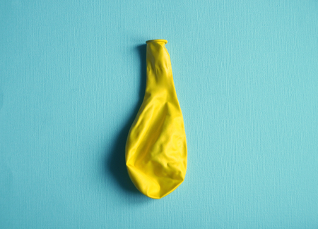 Deflated yellow balloon on blue background Concept photoの写真素材