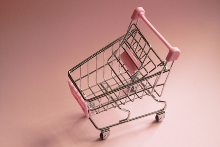 Shopping cart. Empty supermarket trolley on pink background. Consumerism concept photoの写真素材