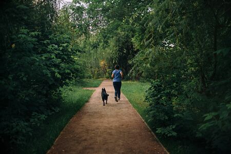 young woman and dog jogging in the park, rear viewの写真素材