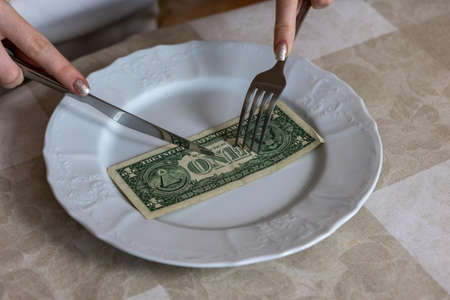 A woman cuts a dollar on a plate with a knife Concept photo