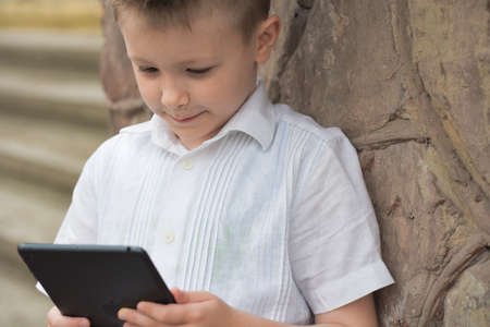 boy with tablet near school with a book online learning