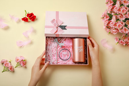 Female hands holding gift box with ring and flowers on beige backgroundの写真素材
