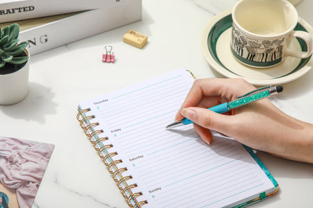 woman's hand writing in notebook on office desk with cup of coffeeの写真素材