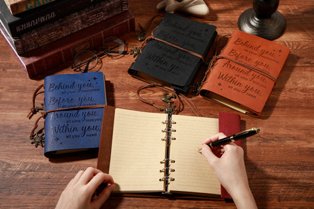 Female hands writing in notebook with old books on wooden table, top viewの写真素材