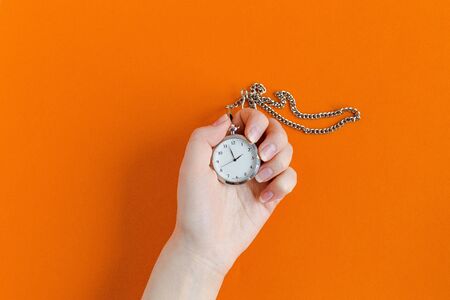 hand holding a clock on orange background. Timeless conceptの写真素材