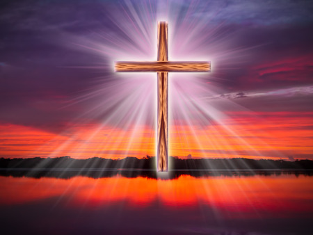 A cross in the sky over a river or coean with light rays at sunrise or sunset.の写真素材