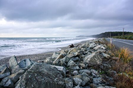 Road parallel to beautiful rocky sea shore. Sea waves pounding shoreline with cloudy sky.