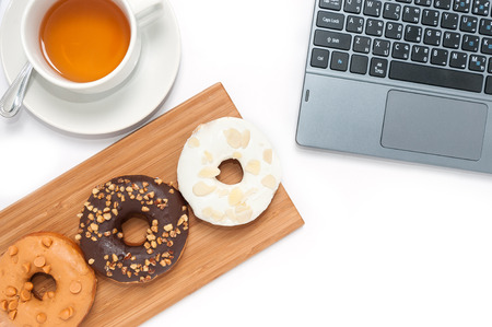 Delicious donuts with icing in wood plate and computer isolated on whiteの写真素材