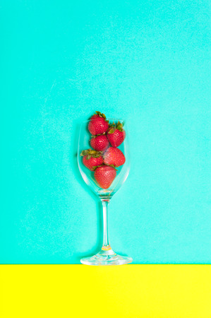 Fresh strawberry in a cup on blue and yellow background. Creative strawberry flat lay.の写真素材