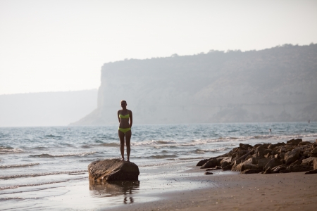 Girl standing on rocky seashore in evening timeの写真素材