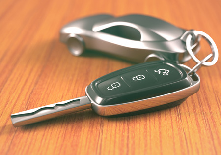 Car key with a car shaped keychain, on a wooden table.