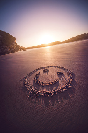 Smiling face drawn on a sandy beach with sundown in the background.の写真素材