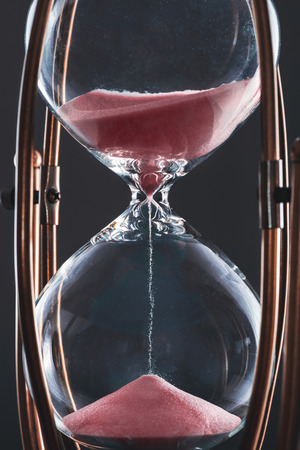 Hourglass with sand in red color and glass body stuck by metal frame.