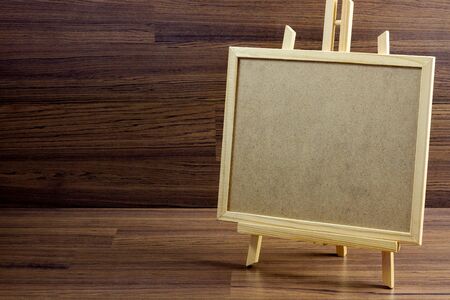 Brown craft board with frame on stand over wooden background.