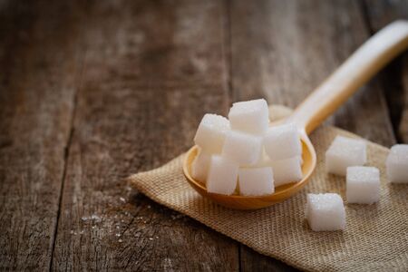 Sugars cube in wooden spoon on jute napkin over wooden background.の写真素材