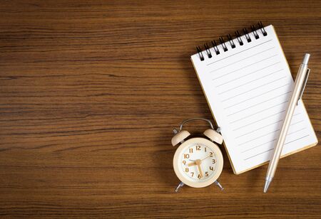 A pen on blank notebook and clock placed beside over wooden background.の写真素材