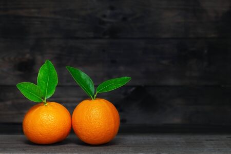 Two oranges with leaves on wooden background.