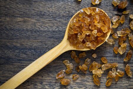 Natural organic brown crystal rock sugar in wooden spoon over wooden background.の写真素材