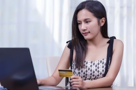 Happy young asian woman smiling and holding credit card while using laptop for shopping online....