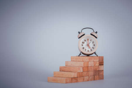 Stacked wooden blocks to develop a ladder for clock on gray background, concept ladder of success has time component.の写真素材