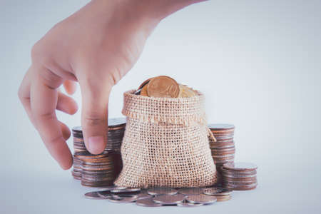 The female hand is picking up coin from the pile of coins and coin in sackcloth.の写真素材