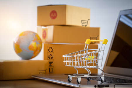 Shopping cart or trolley  on a notebook computer placed in front of the parcel box for delivery to customers. Commercial transactions conducted electronically on the Internet for distance selling.の写真素材
