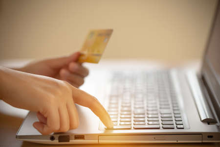 Female hand is pressing the enter button to agree to order online and pay via credit card. Online shopping and spending via credit cards instead of cash to avoid touching concept.の写真素材