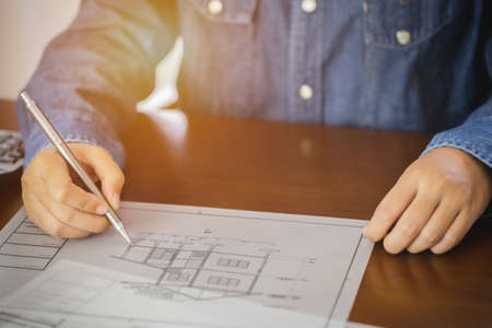 Architect or engineer holding pen pointing construction project equipment on the desk with a blueprint in the office.の写真素材