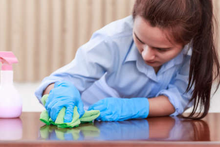 Woman wearing blue protective gloves holding a green microfiber cleaning cloth Cleaning wooden...