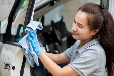 Asian woman hand wearing rubber gloves and using a blue microfiber cloth clean the car interior....