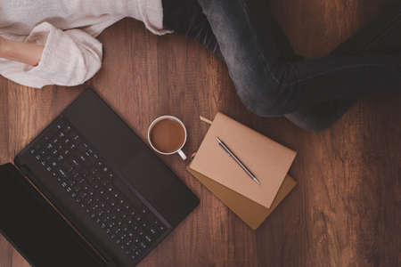 Coffee cup, laptop, notebooks, pencil, and women lying on the wooden floor.