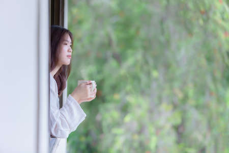 Asian women drinking hot coffee and smoke in the morning sunshine after waking up in the bedroom.