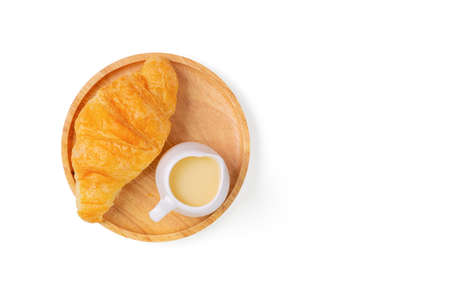 Croissants with sweetened condensed milk on wooden bread cutting board over white background. Croissant french breakfast. Top view.の写真素材