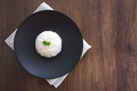 Cooked jasmine rice in black plate and peppermint Leaves with napkin on wooden table. Thai Jasmine rice.の写真素材