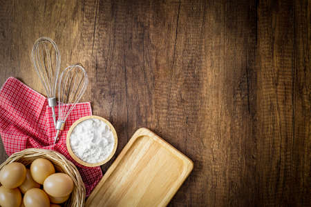 Baking background. Flour in wooden cup, eggs in wicker basket, Egg beater on red placemat and Bread...