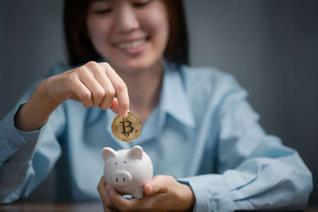 Woman is putting golden bitcoin into the piggy bank.の写真素材